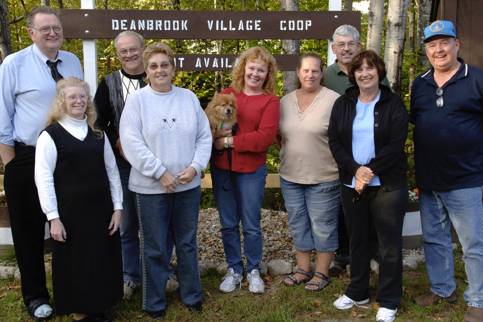 A group of adults stand in front of a sign that reads Deanbrook Village Coop