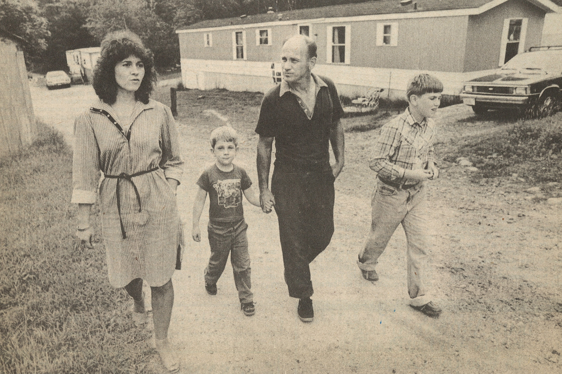 Black and white newspaper photo of a woman walking on gravel street with a man and two young boys