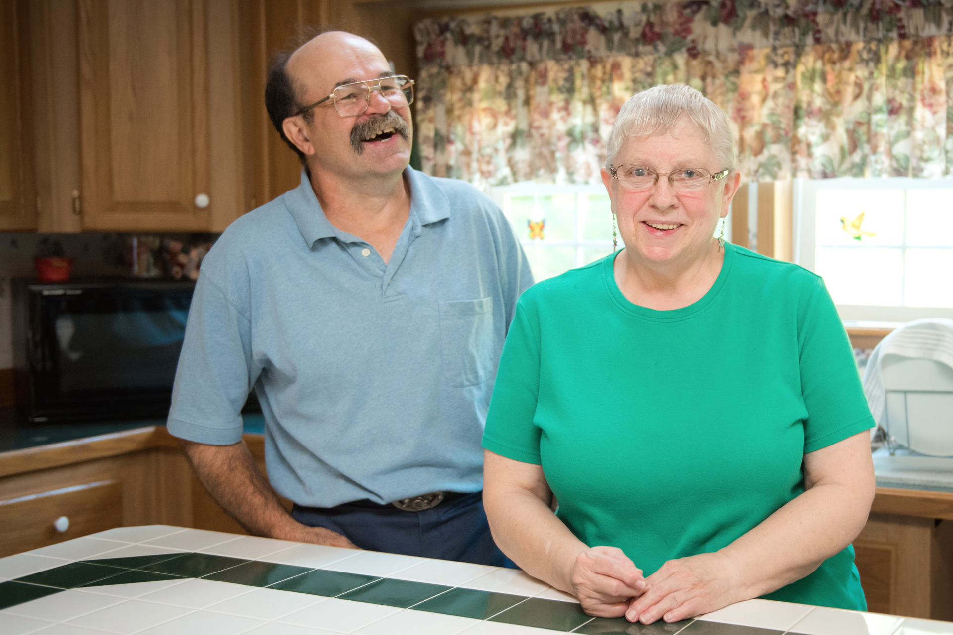 Man and woman stand at kitchen counter; man is laughing