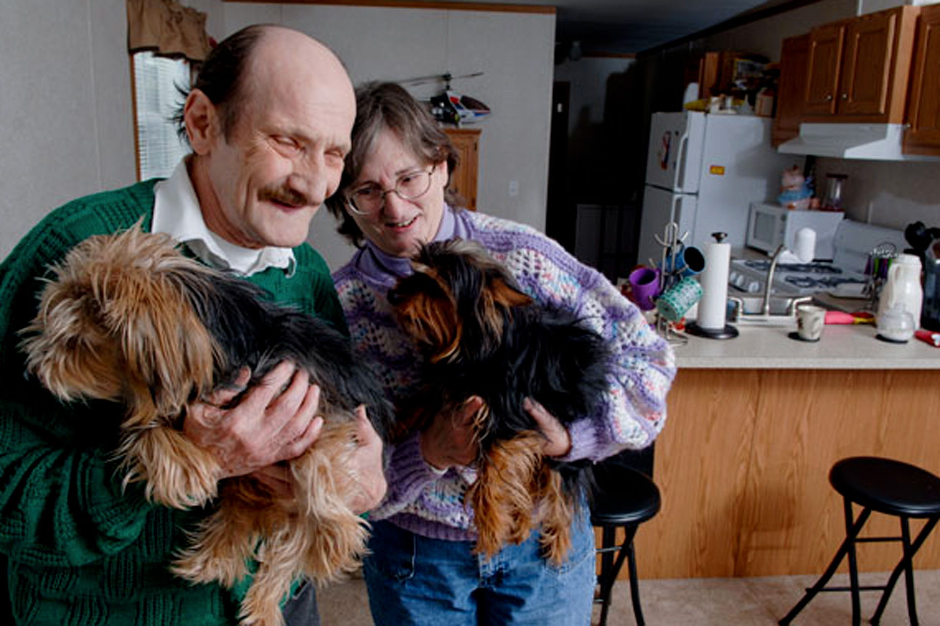 Man and woman holding squirmy dogs in their kitchen