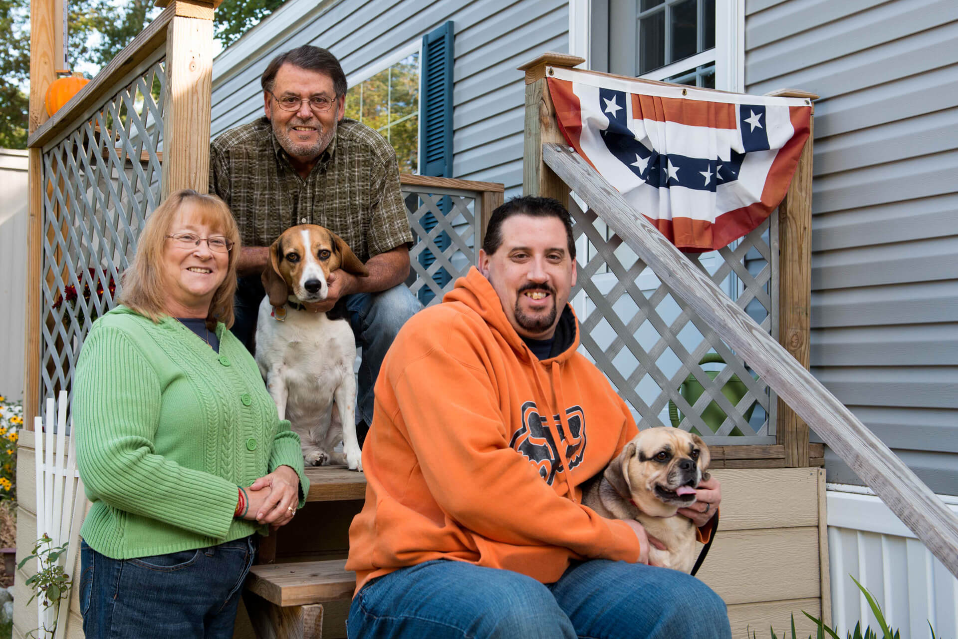 Two men, a woman and two dogs pose on steps to a manufactured home.